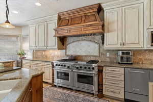 Kitchen featuring cream cabinetry, appliances with stainless steel finishes, a textured ceiling, dark stone countertops, and backsplash