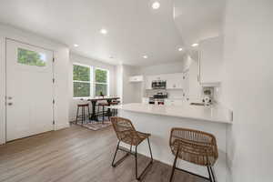 Kitchen featuring a breakfast bar, white cabinetry, a peninsula, recessed lighting, and light wood finished floors