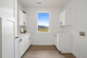 Laundry area with a mountain view, light wood-style floors, cabinet space, and washer hookup