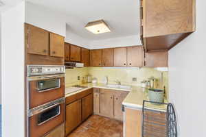 Kitchen with light countertops, brown cabinetry, black electric cooktop, and under cabinet range hood
