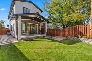 Back of property with a fenced backyard, a ceiling fan, board and batten siding, a wooden deck, and a patio