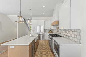 Kitchen featuring tasteful backsplash, high end appliances, pendant lighting, white cabinetry, and light stone countertops