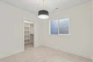 Unfurnished bedroom featuring light carpet and a walk in closet