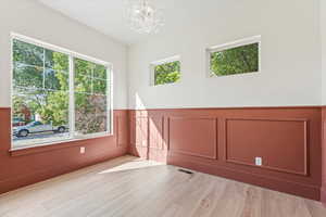 Empty room with a wainscoted wall, a decorative wall, a chandelier, and light wood finished floors