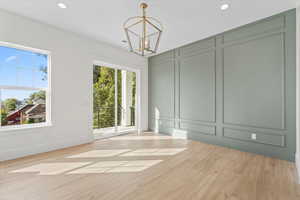 Unfurnished dining area with a decorative wall, light wood-style floors, recessed lighting, and a chandelier