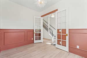 Spare room featuring stairway, french doors, a decorative wall, a wainscoted wall, and wood finished floors