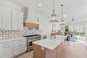 Kitchen with an island with sink, double oven range, backsplash, custom range hood, and pendant lighting