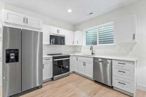 Kitchen with stainless steel appliances, white cabinetry, light wood finished floors, and recessed lighting