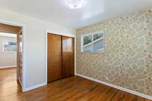 Unfurnished bedroom featuring wallpapered walls, hardwood / wood-style flooring, and a closet