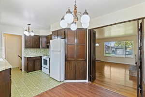 Kitchen with dark brown cabinetry, a chandelier, light countertops, hanging light fixtures, and white appliances