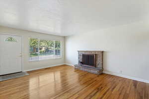 Unfurnished living room featuring a brick fireplace, wood finished floors, and a textured ceiling