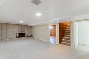 Unfurnished living room featuring light colored carpet, a brick fireplace, and stairs
