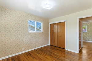 Unfurnished bedroom with wallpapered walls, hardwood / wood-style flooring, and a closet
