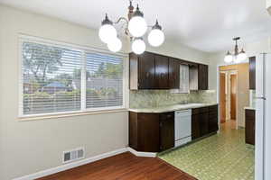 Kitchen with dark brown cabinets, a chandelier, light countertops, backsplash, and light wood-style floors