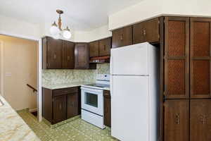 Kitchen with dark brown cabinetry, white appliances, light countertops, and backsplash