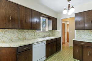 Kitchen with dark brown cabinetry, light countertops, white dishwasher, decorative backsplash, and hanging light fixtures