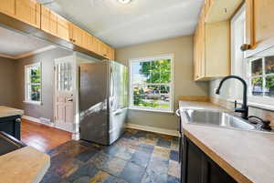 Kitchen featuring freestanding refrigerator, light countertops, light brown cabinetry, stone tile flooring, and crown molding