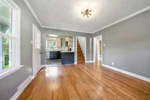 Unfurnished living room with stairway, crown molding, a textured ceiling, dark wood-style flooring, and a chandelier