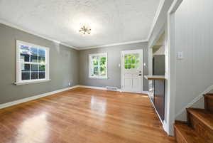 Foyer with ornamental molding, light wood finished floors, a textured ceiling, and stairway