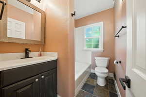 Bathroom with vanity, dark stone finish floors, a textured wall, and tub / shower combination