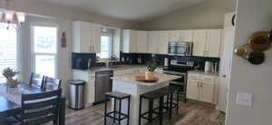 Kitchen with decorative backsplash, vaulted ceiling, appliances with stainless steel finishes, white cabinets, and dark wood-style floors