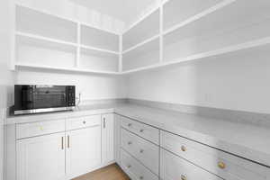 Kitchen with stainless steel microwave, light stone counters, light wood-type flooring, and white cabinetry