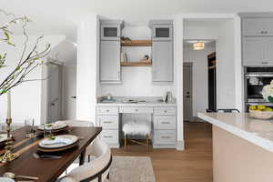 Kitchen featuring light wood-style flooring, light stone countertops, stainless steel double oven, gray cabinets, and open shelves
