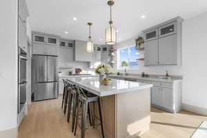 Kitchen with open shelves, light wood-style floors, decorative light fixtures, appliances with stainless steel finishes, and a breakfast bar