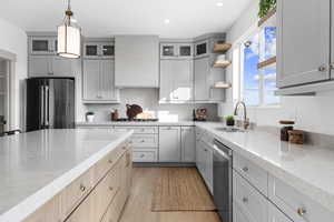 Kitchen with open shelves, light stone countertops, hanging light fixtures, light brown cabinets, and stainless steel appliances