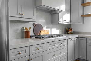 Kitchen with light stone counters, open shelves, wall chimney exhaust hood, and gray cabinetry