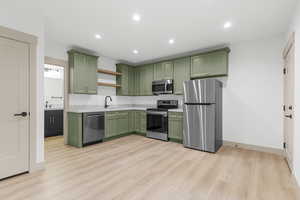 Kitchen with green cabinetry, stainless steel appliances, recessed lighting, light wood-style floors, and open shelves