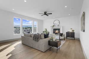 Living room with light wood-style floors, recessed lighting, a glass covered fireplace, and ceiling fan