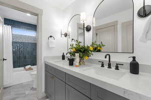 Bathroom featuring shower / bath combo with shower curtain, double vanity, and light marble finish flooring