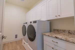 Laundry area featuring light wood finished floors, cabinet space, and washer and clothes dryer