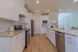 Kitchen with appliances with stainless steel finishes, white cabinetry, premium range hood, light stone counters, and recessed lighting