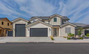 View of front of home with stone siding, an attached garage, driveway, and stucco siding
