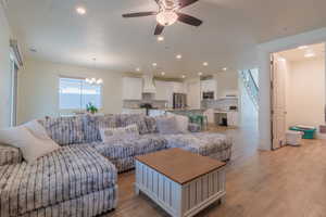 Living area with light wood-style floors, a ceiling fan, a chandelier, and recessed lighting
