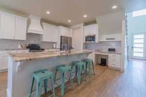 Kitchen featuring white cabinets, premium range hood, decorative backsplash, a breakfast bar area, and stainless steel appliances