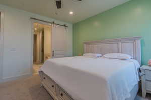 Bedroom with light carpet, recessed lighting, a barn door, ceiling fan, and ensuite bath