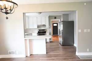 Kitchen featuring light countertops, appliances with stainless steel finishes, white cabinetry, light wood-style flooring, and a peninsula