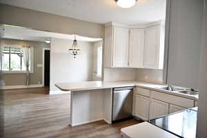 Kitchen featuring light countertops, dishwasher, light wood-style floors, white cabinets, and a textured ceiling