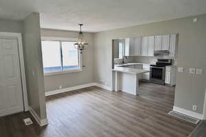 Kitchen with light countertops, stainless steel range with electric cooktop, decorative light fixtures, white cabinetry, and a chandelier