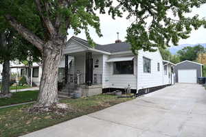 View of front of house featuring an outbuilding, a detached garage, concrete driveway, a chimney, and a shingled roof
