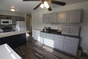 Kitchen featuring white appliances, gray cabinetry, dark wood-style floors, light countertops, and a ceiling fan