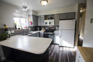 Kitchen with white appliances, gray cabinetry, open shelves, light countertops, and dark wood-type flooring