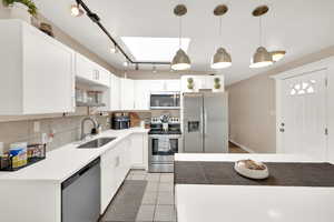 Kitchen with stainless steel appliances, a skylight, white cabinetry, and light tile patterned flooring
