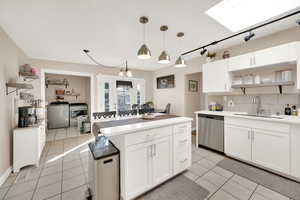 Kitchen featuring white cabinetry, light tile patterned flooring, light countertops, a skylight, and decorative backsplash
