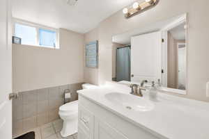 Full bath with vanity, light tile patterned floors, tile walls, and curtained shower