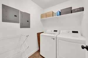Washroom featuring electric panel, washer and clothes dryer, and light wood-type flooring