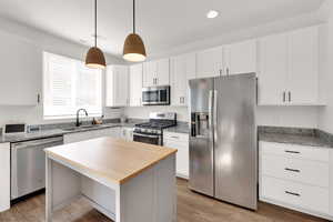 Kitchen with stainless steel appliances, light wood-type flooring, light stone counters, white cabinets, and recessed lighting